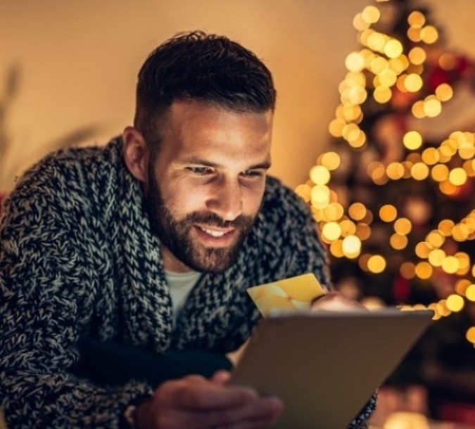 man holding card and tablet in front of a christmas tree